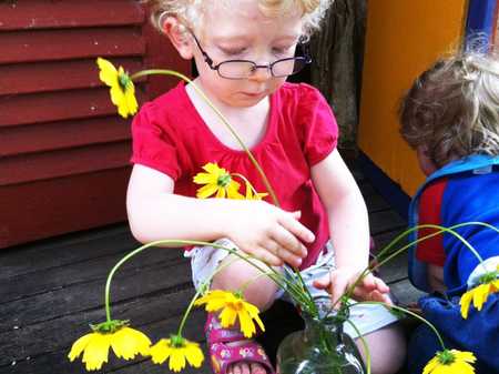 child arranging bright yellow flowers in a glass bottle