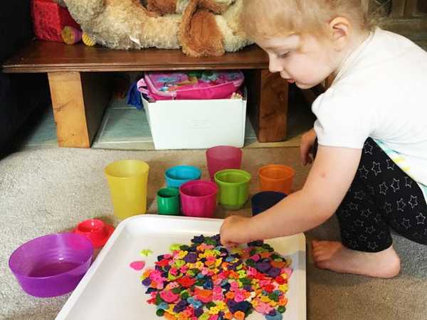 child sorting multicoloured buttons into colourful containers