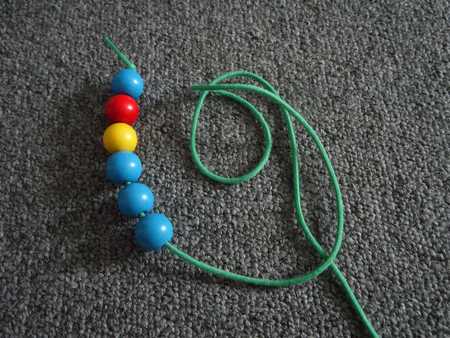 child threading orange beads onto a thin blue string