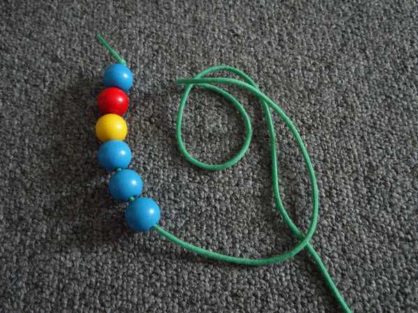 child threading orange beads onto a thin blue string