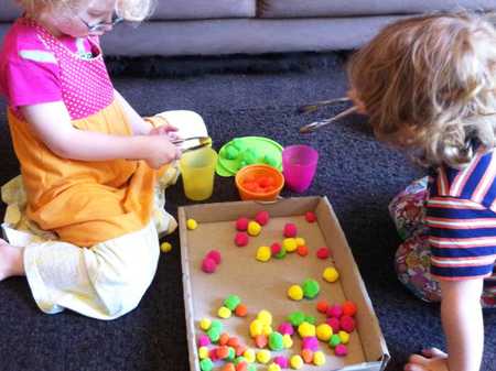 two young children using tongs to place multicoloured pompoms into colourful containers